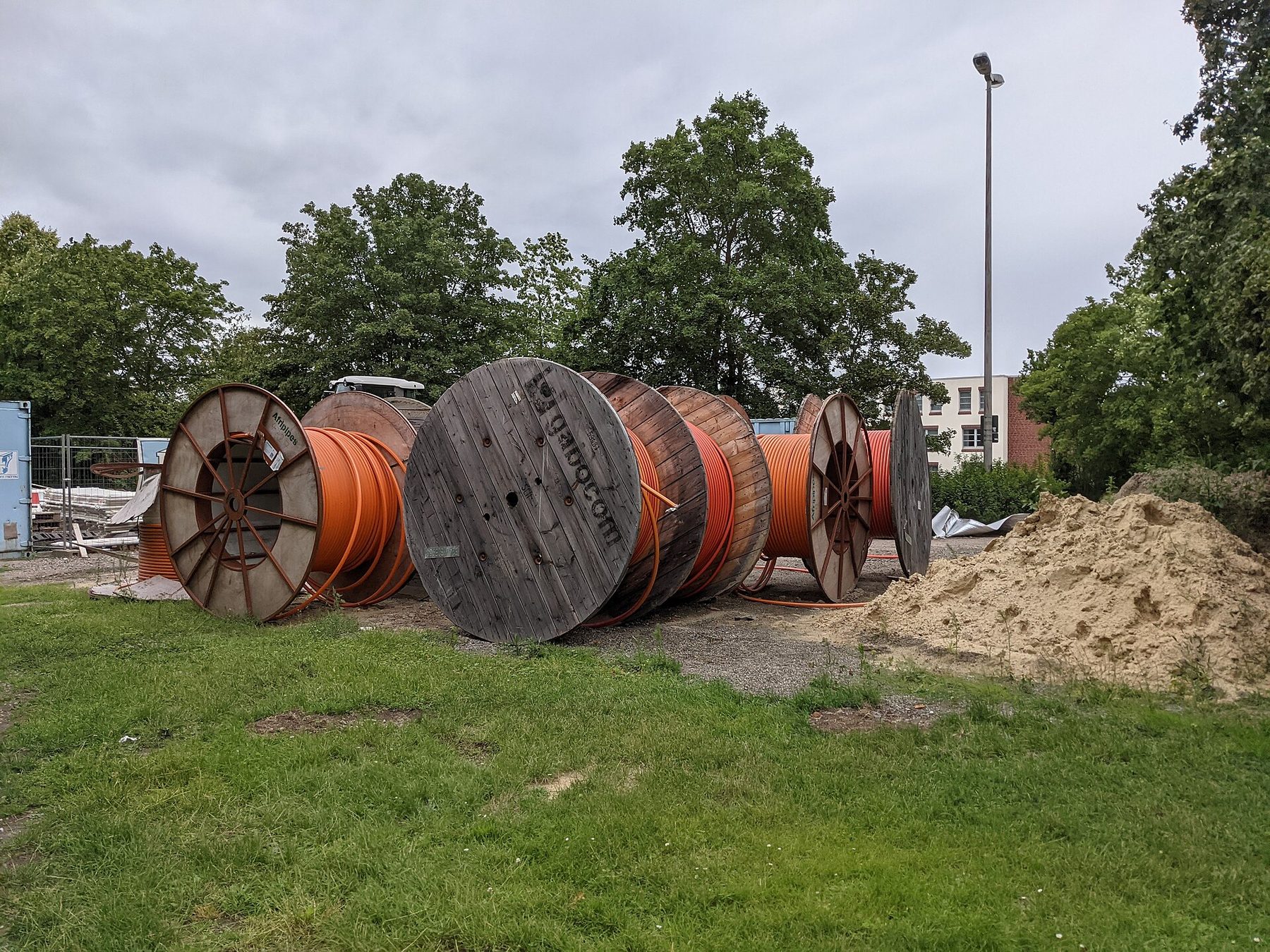 Glasfaser-Baustelle mit großen Kabeltrommeln und orangefarbenen Leerrohren für den Breitbandausbau