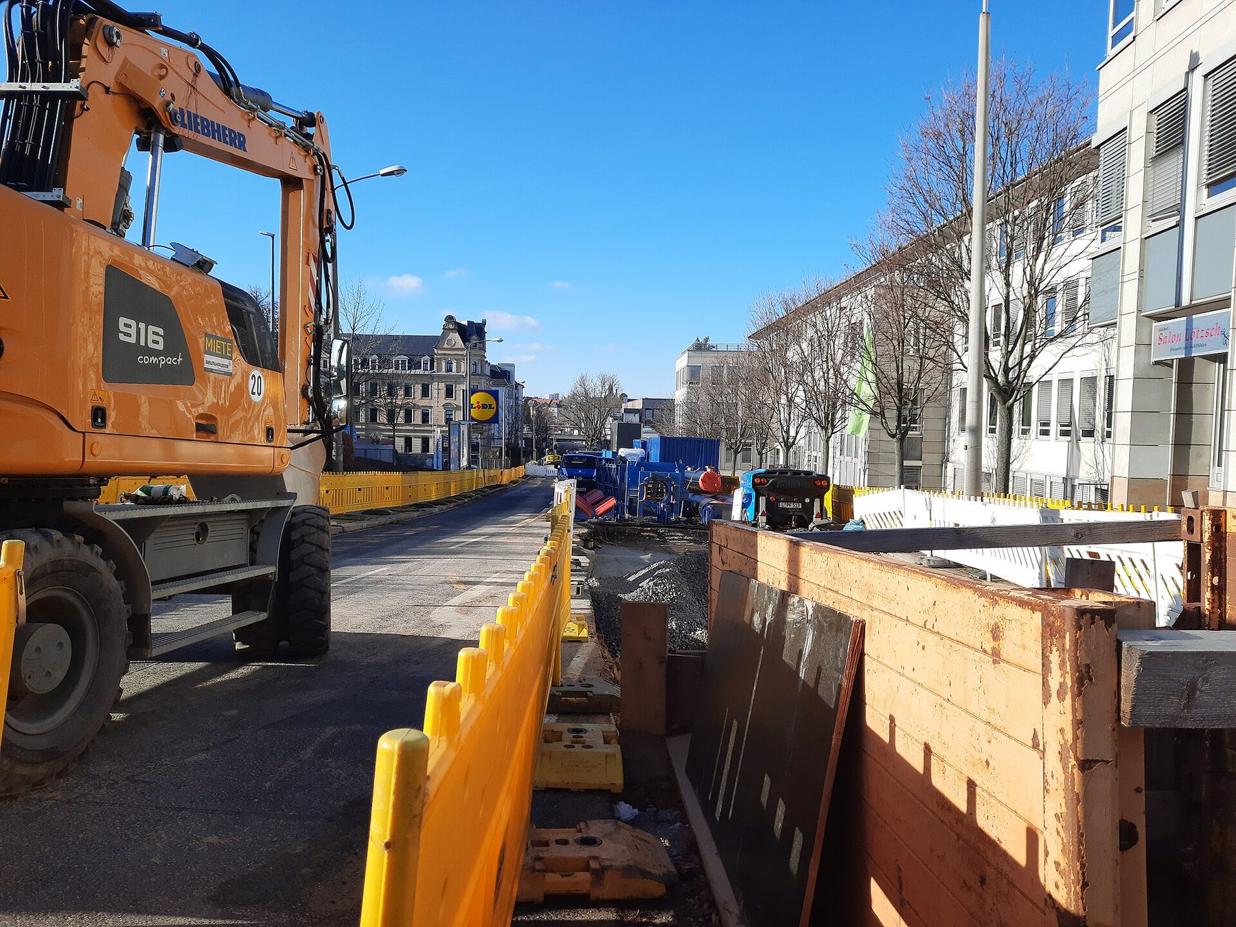 Tiefbaustelle im Straßenbereich mit Bagger und verbautem Leitungsgraben für Trassenbau und Hausanschlüsse